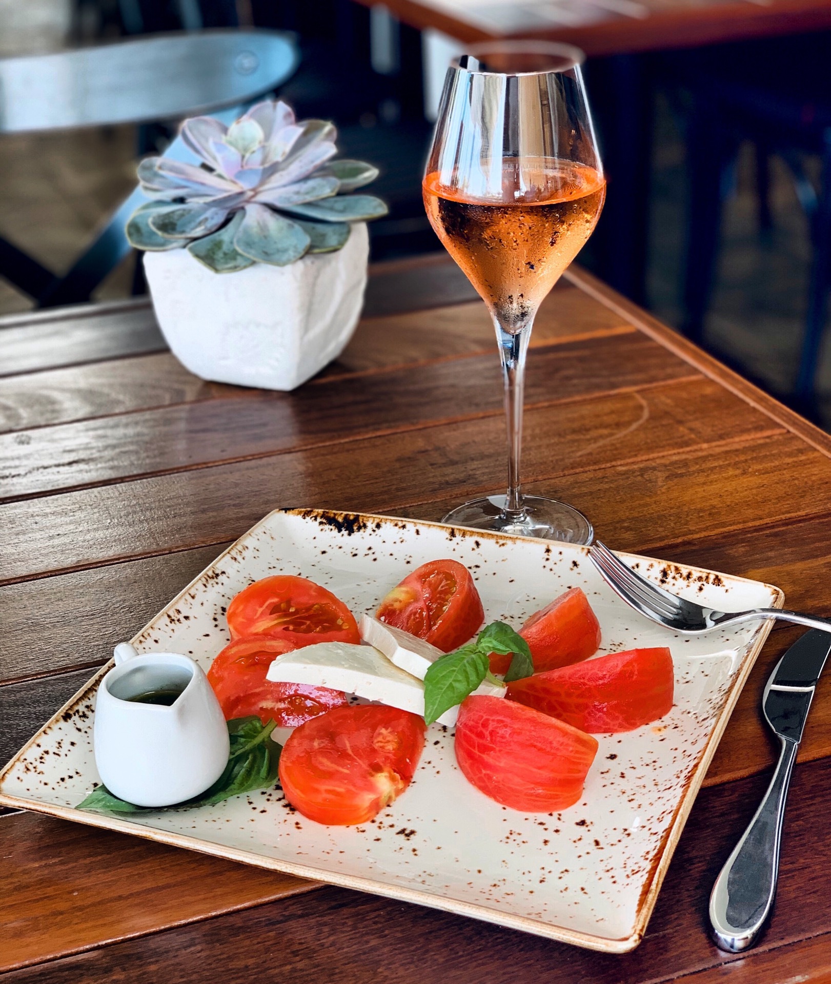 closeup salad with cheese tomatoes square plate with alcoholic beverage near plant